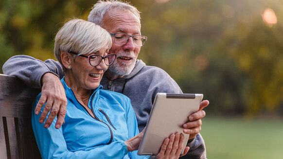 Älteres Paar auf Bank schaut auf Tablet | Quelle: © lordn / Adobe Stock
